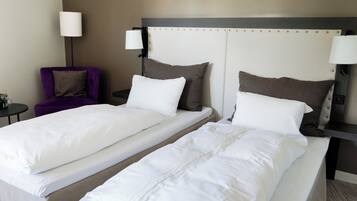 A hotel room with two single beds, a purple armchair, a small table, and a lamp.