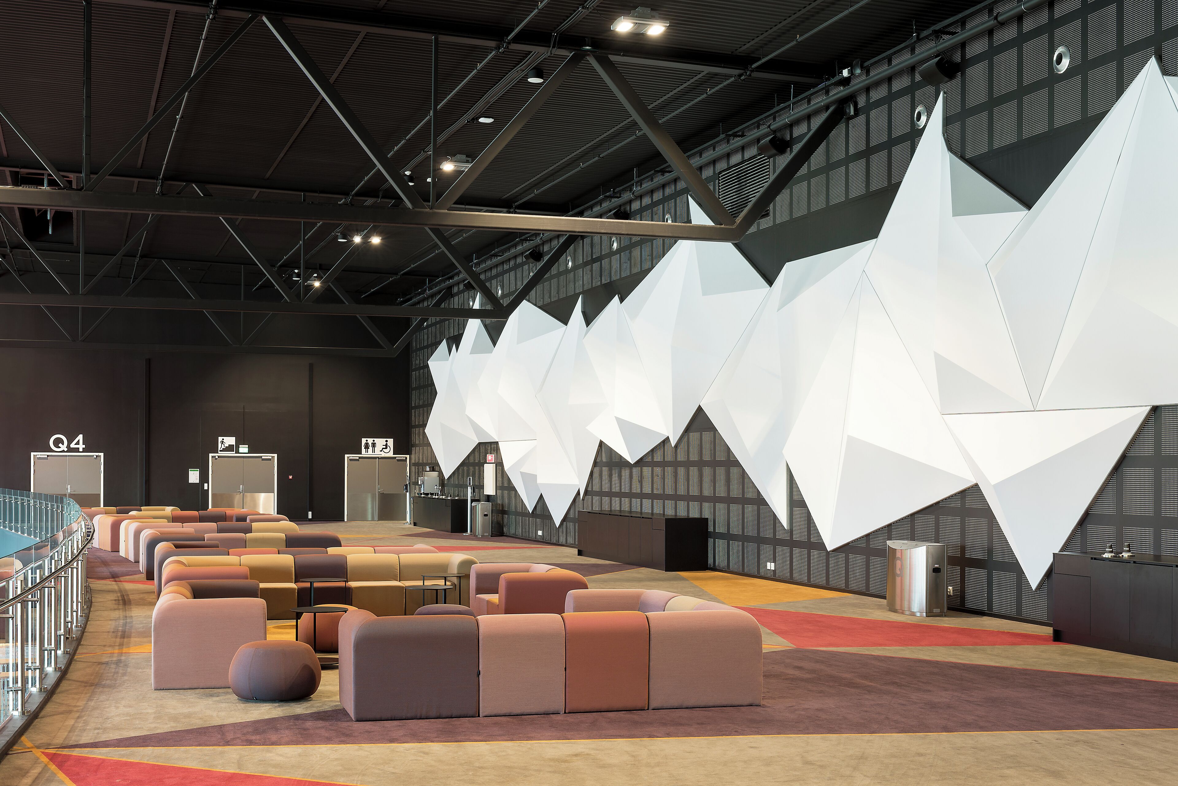 A modern conference room with a high ceiling, geometric white wall panels, and a seating area with cushioned chairs.