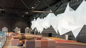 A modern conference room with a high ceiling, geometric white wall panels, and a seating area with cushioned chairs.