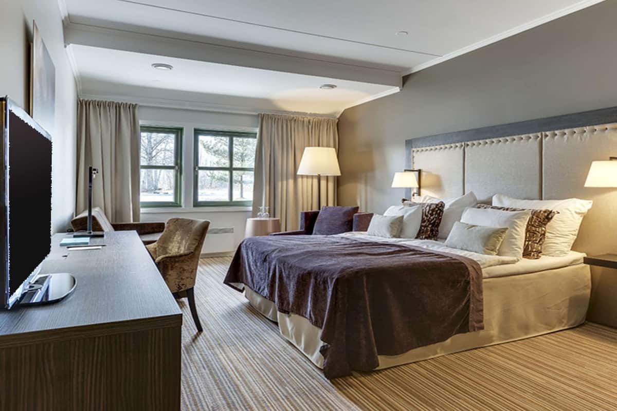 Una habitación de hotel con cama, lámparas de noche, un escritorio con computadora y una silla.