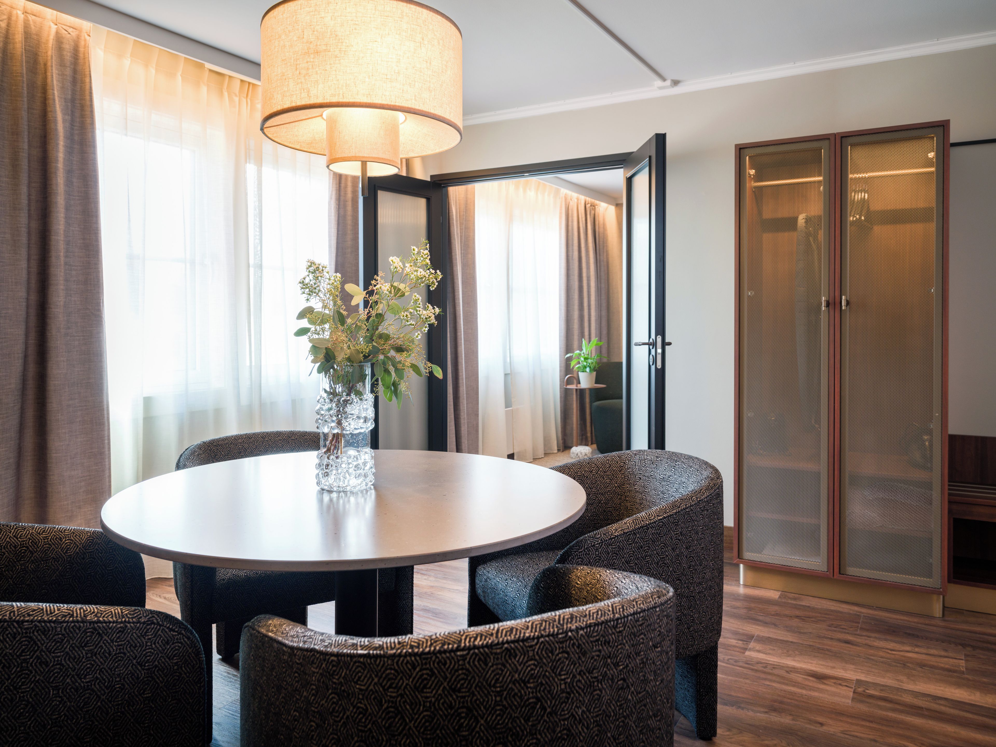 A modern dining area with a round table, patterned chairs, a vase with flowers, and a large lamp.