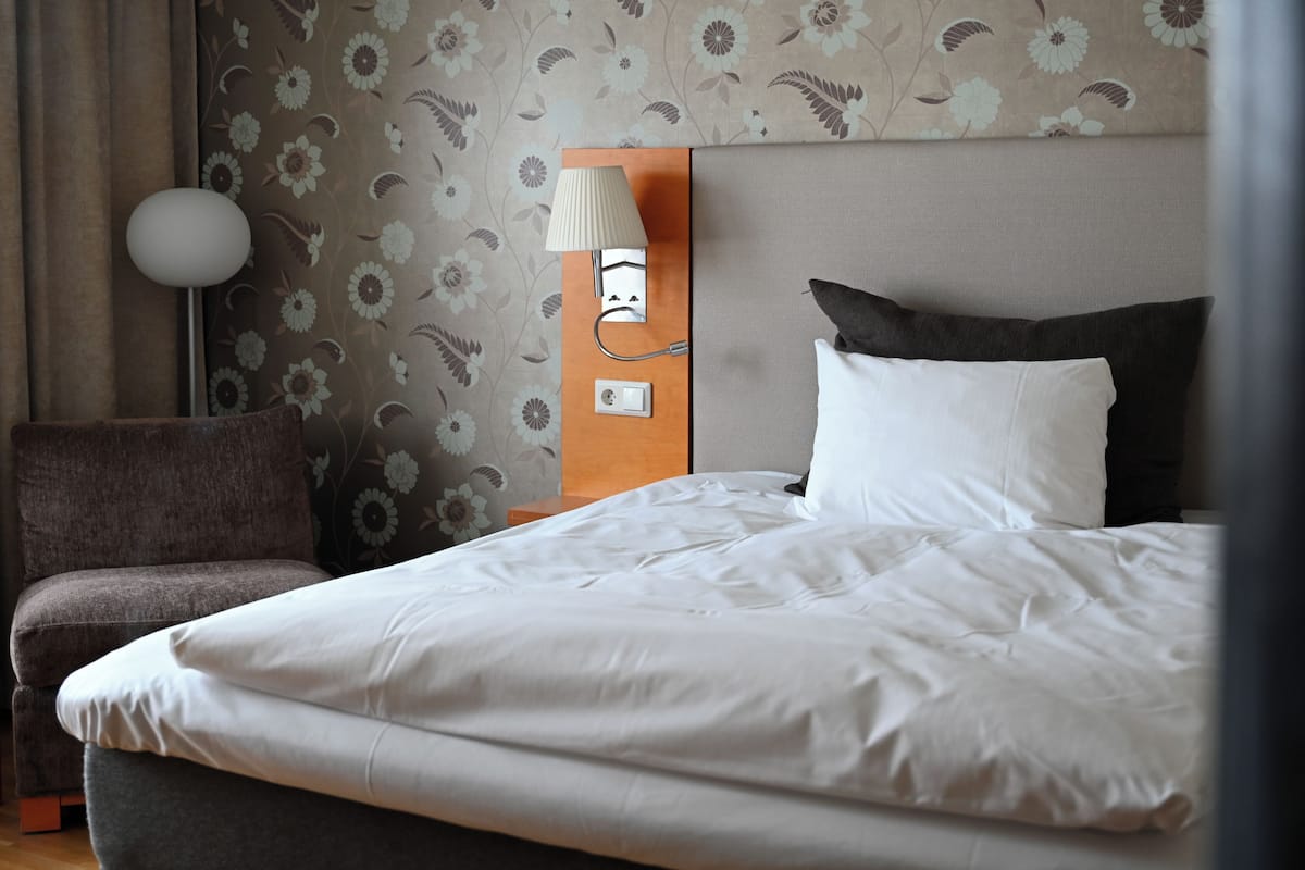 Una habitación de hotel con cama, mesita de noche, lámpara y silla.