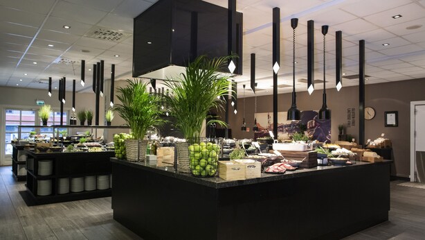 Un espace cuisine moderne doté d’un îlot central, de plans de travail noirs et de luminaires suspendus.