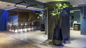 Un hall d’entrée moderne avec un comptoir d’accueil en bois, de grandes plantes en pot et un sol carrelé.