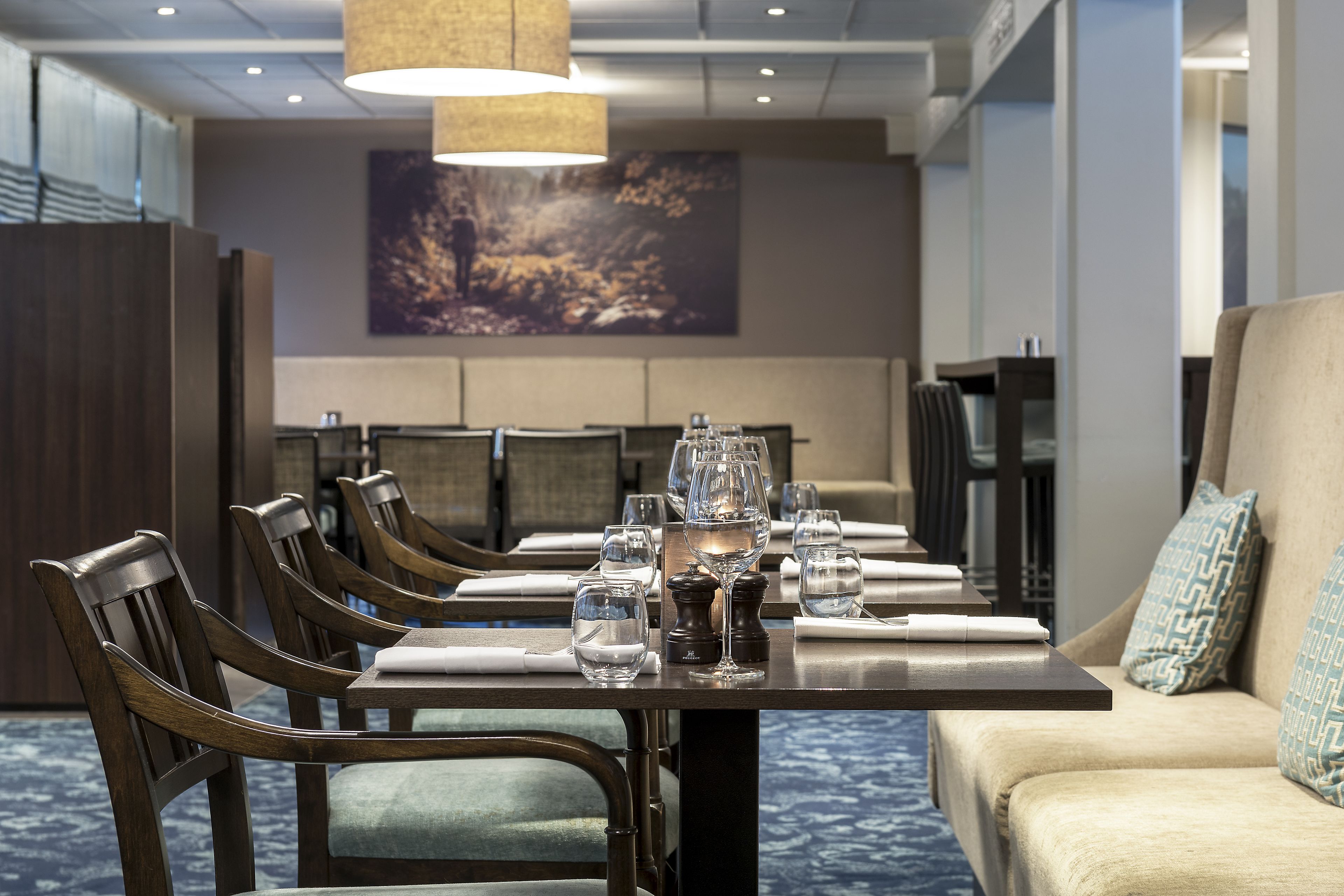 A dining area with a long table set for six, wooden chairs, and a sofa with patterned cushions.