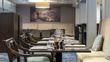 A dining area with a long table set for six, wooden chairs, and a sofa with patterned cushions.