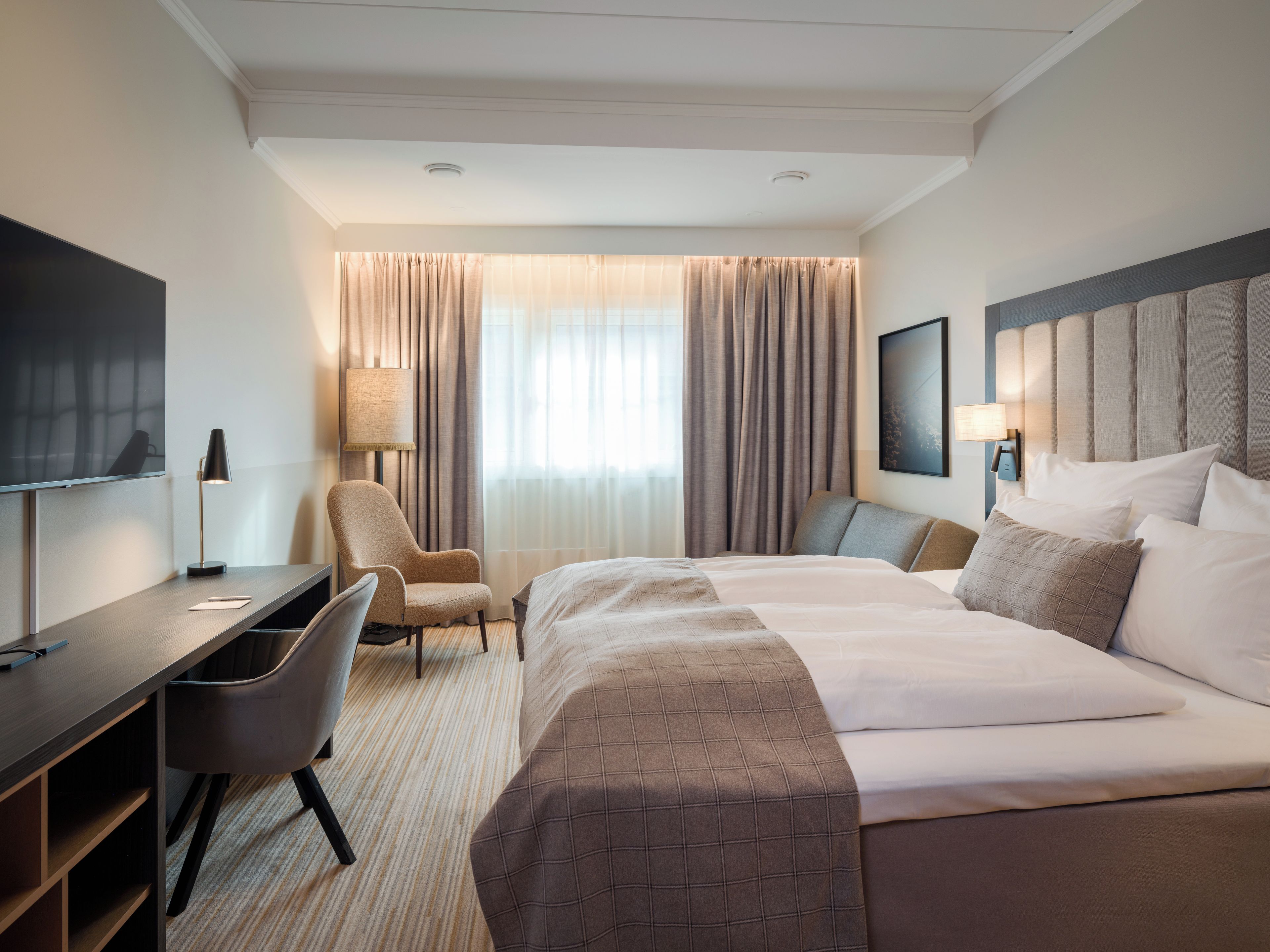 A hotel room with a bed, desk, chair, and a TV.