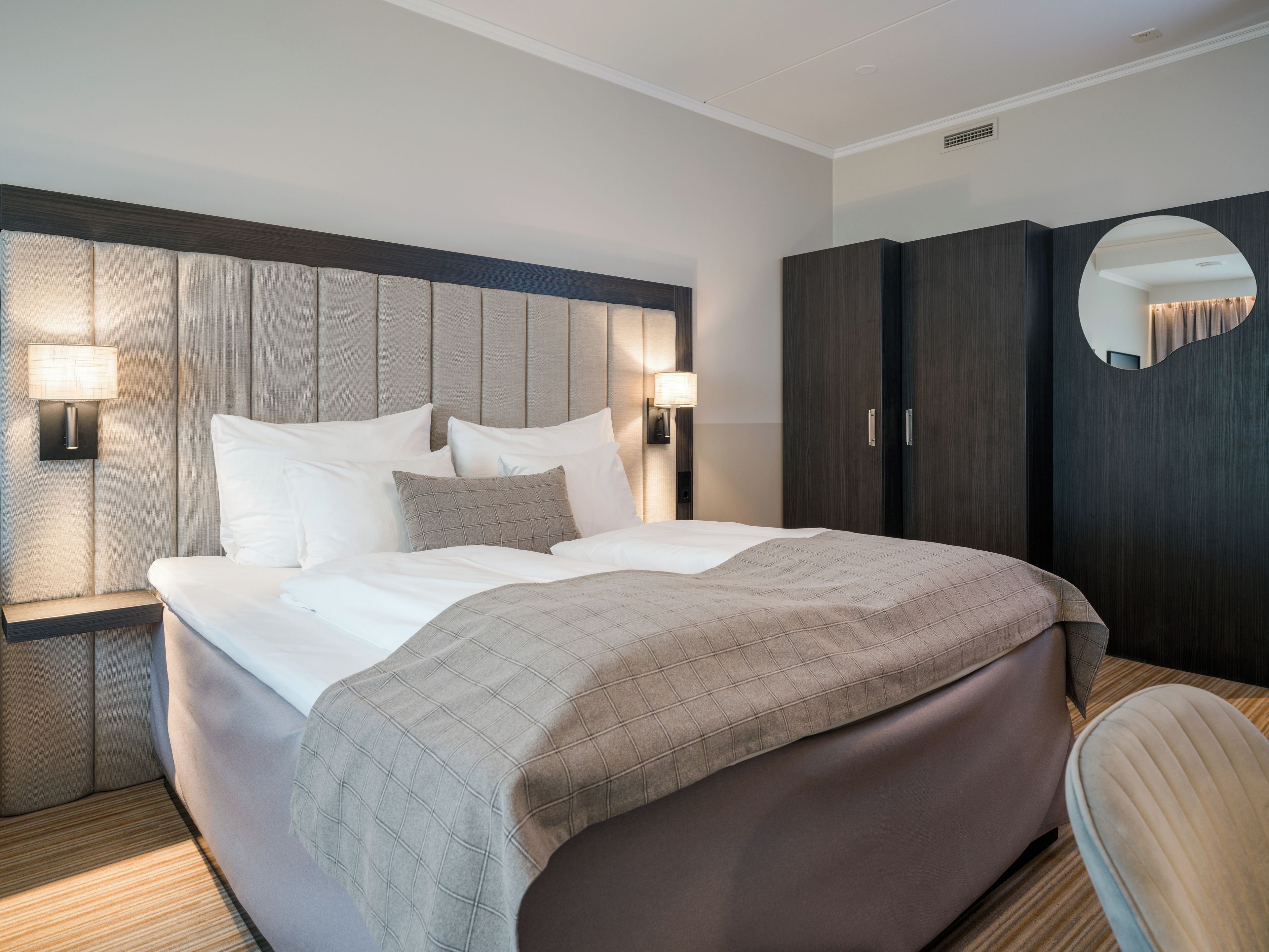 Une chambre d’hôtel avec un grand lit, deux lampes de chevet, une armoire et un miroir.