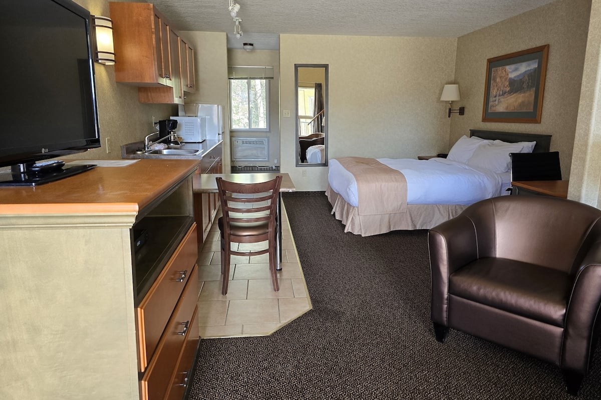 Habitación de hotel con kitchenette, una cama, una silla y un televisor.