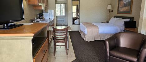Habitación de hotel con kitchenette, una cama, una silla y un televisor.