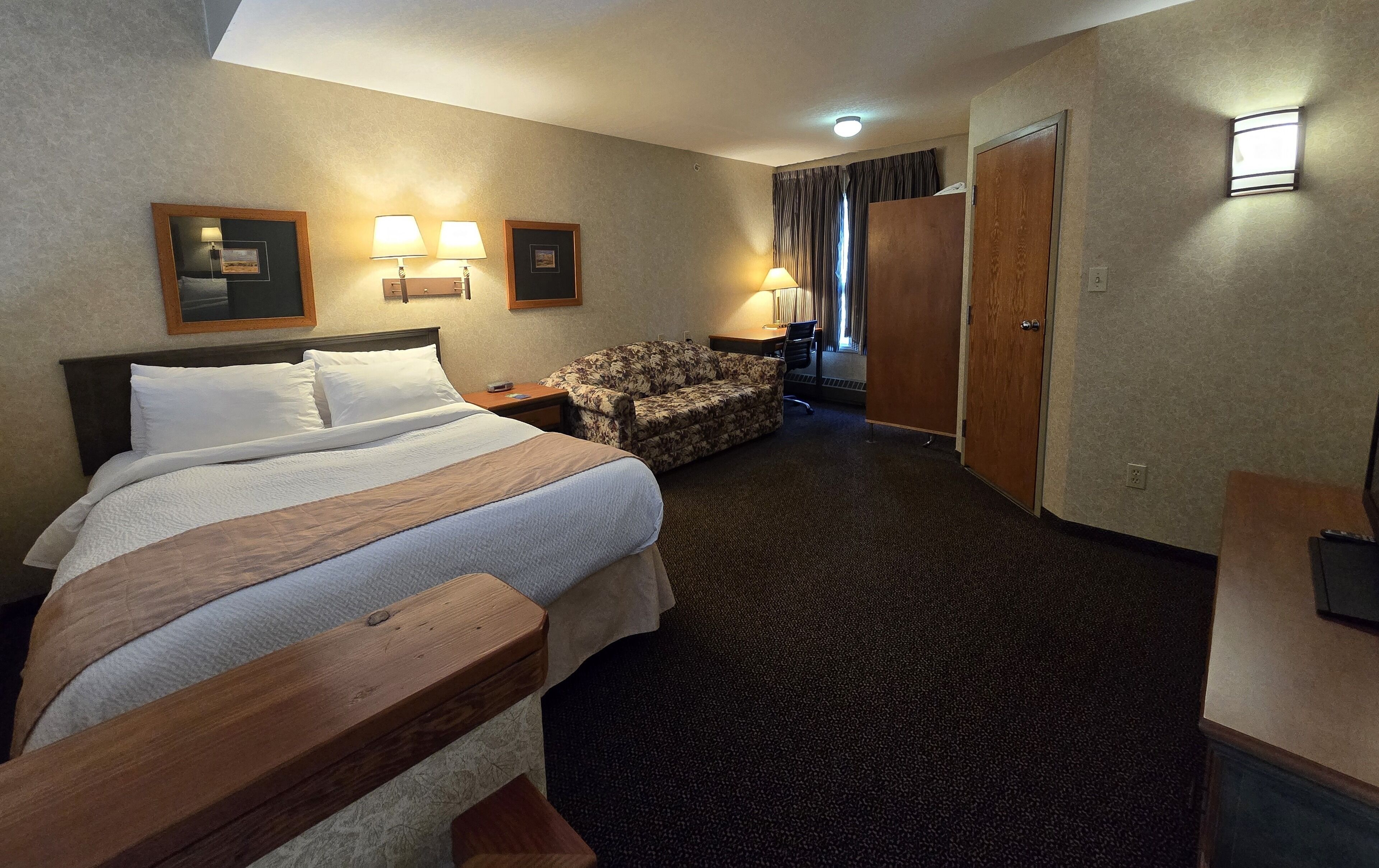 A hotel room with a large bed, a wooden bench, a sofa, a desk, and a wardrobe.