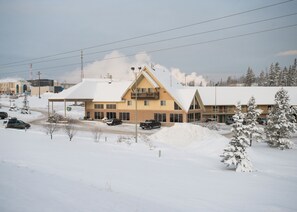 A hotel with a large snow-covered parking lot, a covered outdoor area, and a building with a prominent triangular roof.