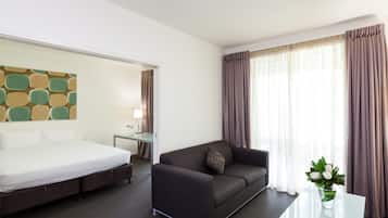 A hotel room with a bed, a sofa, a small table, a lamp, and a window with curtains.