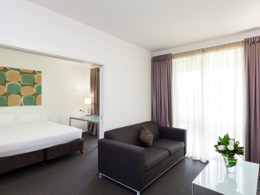 Una habitación de hotel con una cama, un sofá, una mesita, una lámpara y una ventana con cortinas.