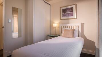 A neatly made bed with a white headboard, a bedside lamp, and a framed picture on the wall.