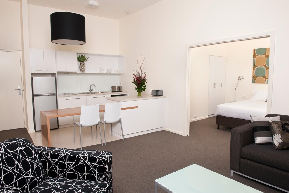 A compact living space with a kitchenette, a dining area, a bed, and a sofa.
