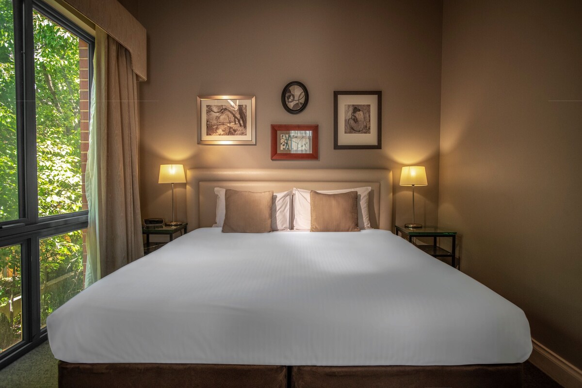 A neatly made bed with a white duvet, two bedside lamps, and framed artwork on the wall.