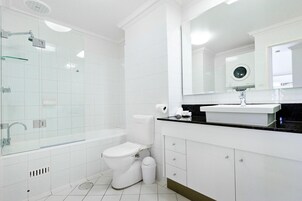 Un baño moderno con ducha de vidrio, inodoro blanco y encimera negra con lavamanos.
