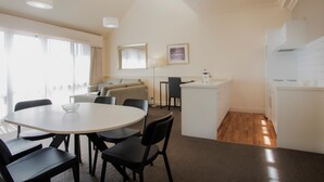 Una cocina moderna con armarios blancos, un comedor con mesa y sillas redondas, y una sala de estar con sofá y una lámpara.