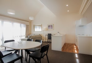 Una cocina moderna con armarios blancos, un comedor con mesa y sillas redondas, y una sala de estar con sofá y una lámpara.