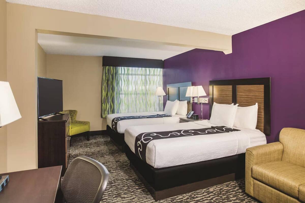 A hotel room with a large bed, a desk, a chair, a TV, and a window with curtains.
