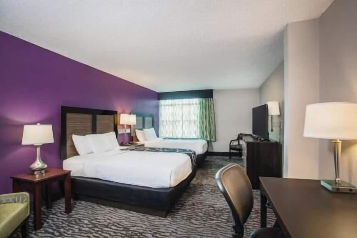 A hotel room with a bed, a desk, a chair, a TV, and a window with curtains.