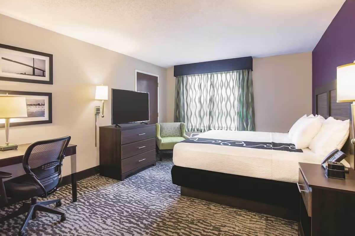 A hotel room with a bed, desk, chair, TV, and curtains.