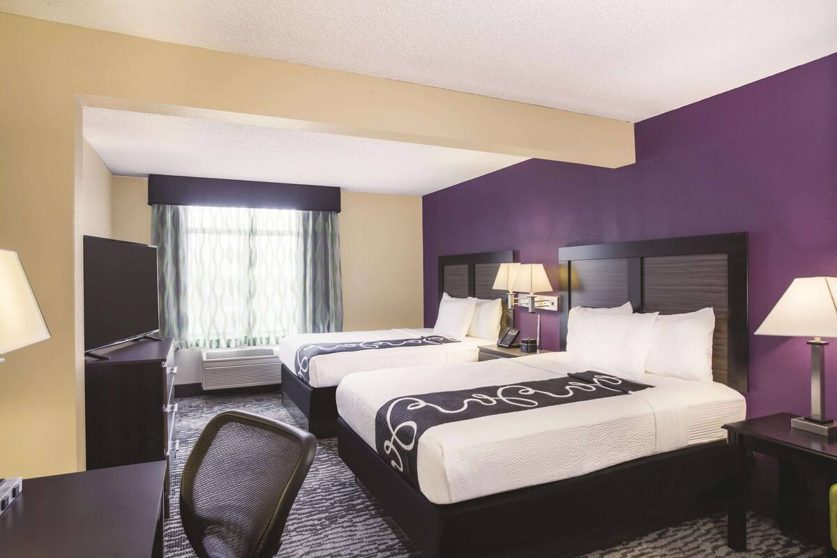 A hotel room with two beds, a desk, a chair, a TV, and a window with curtains.