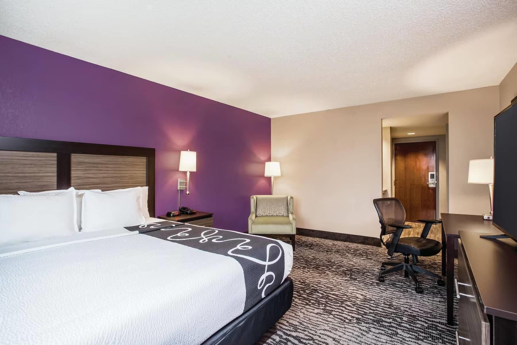 Una habitación de hotel con una cama, un escritorio, una silla y una puerta.
