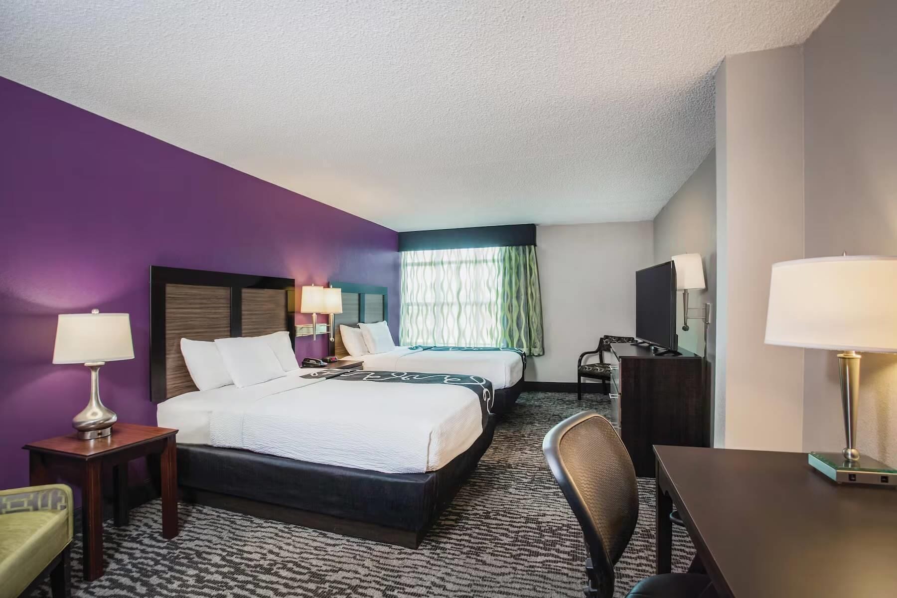 Ein Hotelzimmer mit einem großen Bett, zwei Nachttischen, einem Schreibtisch, einem Sessel und einem Fernseher.