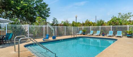 A swimming pool with a white fence, blue lounge chairs, and a metal ladder.