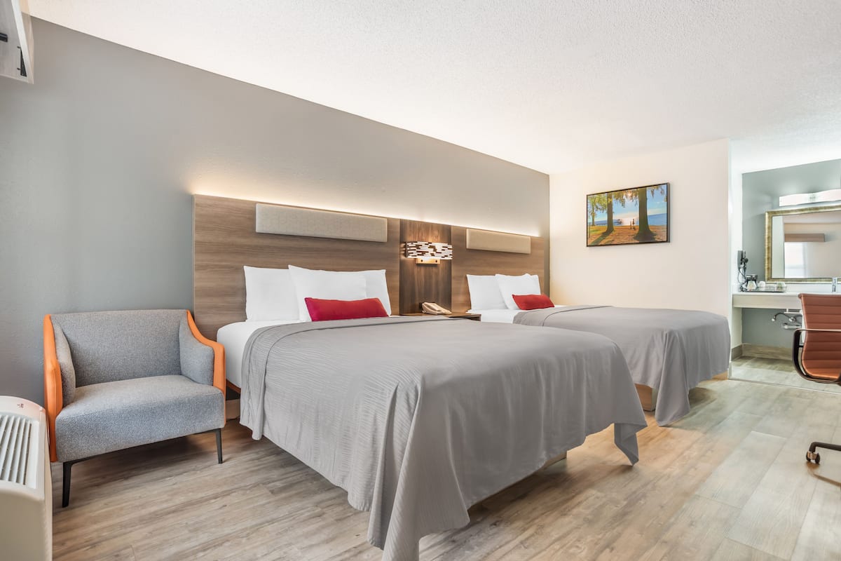 A hotel room with two beds, a chair, a desk, and a painting on the wall.