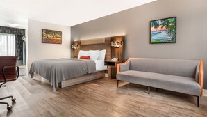 A hotel room with a bed, a sofa, a desk, and two wall-mounted lamps. - Key West Inn Fairhope Al (Fairhope)