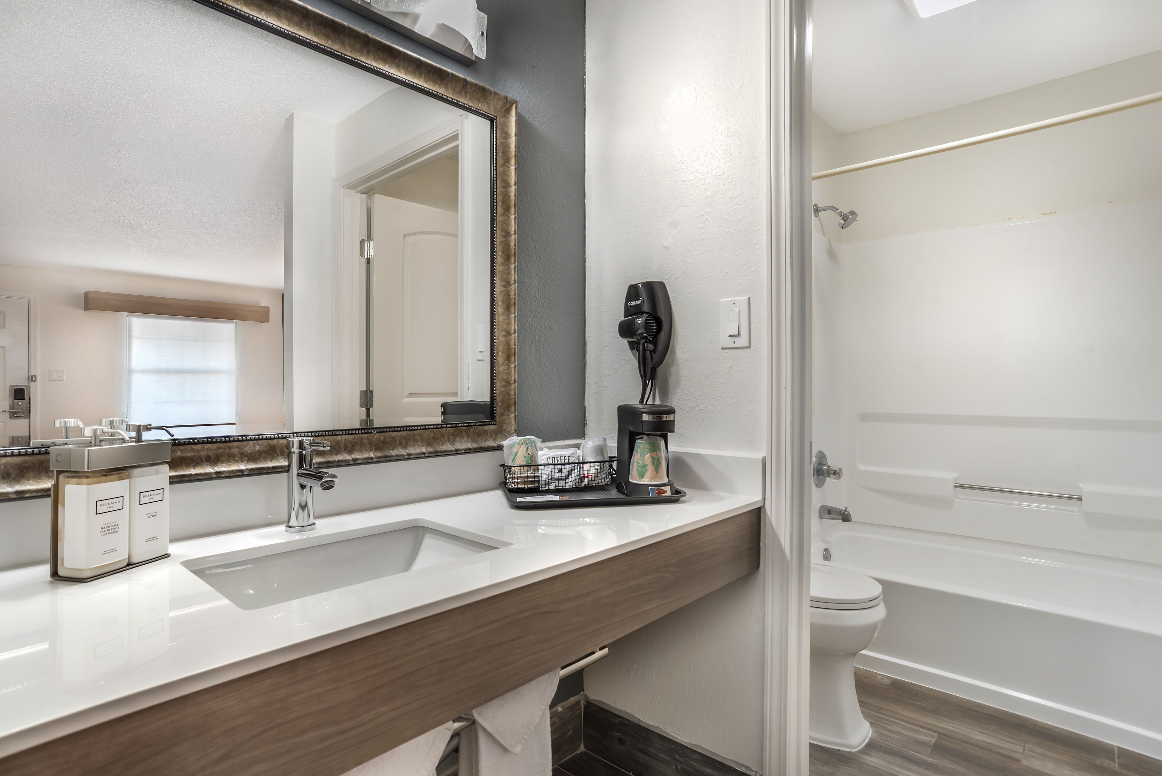 Un baño con lavamanos blanco, espejo, cafetera y bañera.