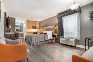 A modern hotel room with a bed, a desk, a chair, and a small kitchenette. - Key West Inn Fairhope Al (Fairhope)
