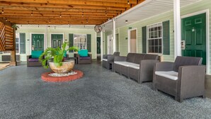 A covered outdoor seating area with wicker furniture, a central plant, and a wooden ceiling with string lights. - Key West Inn Fairhope Al (Fairhope)