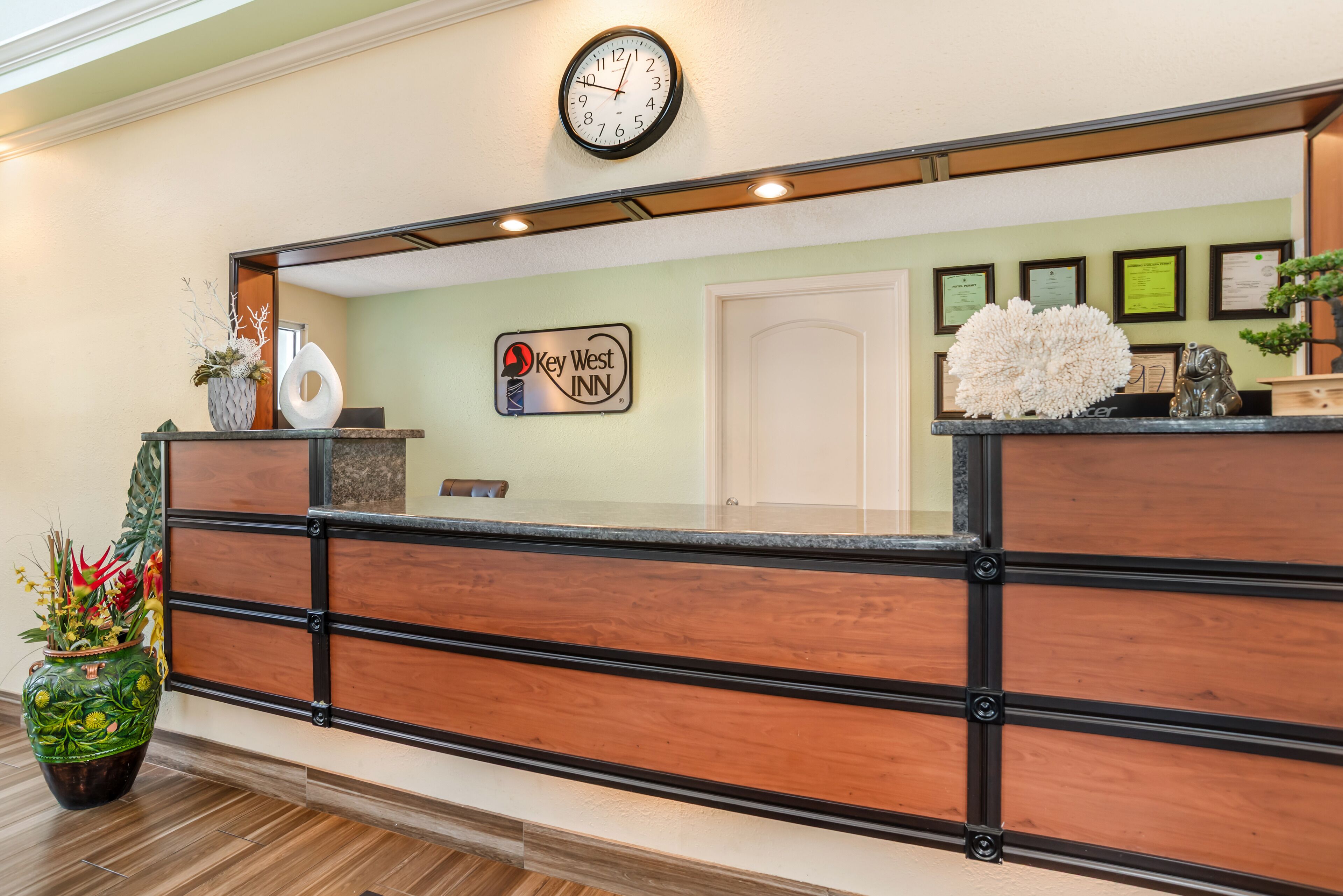 A reception desk with a clock, framed certificates, and a potted plant.
