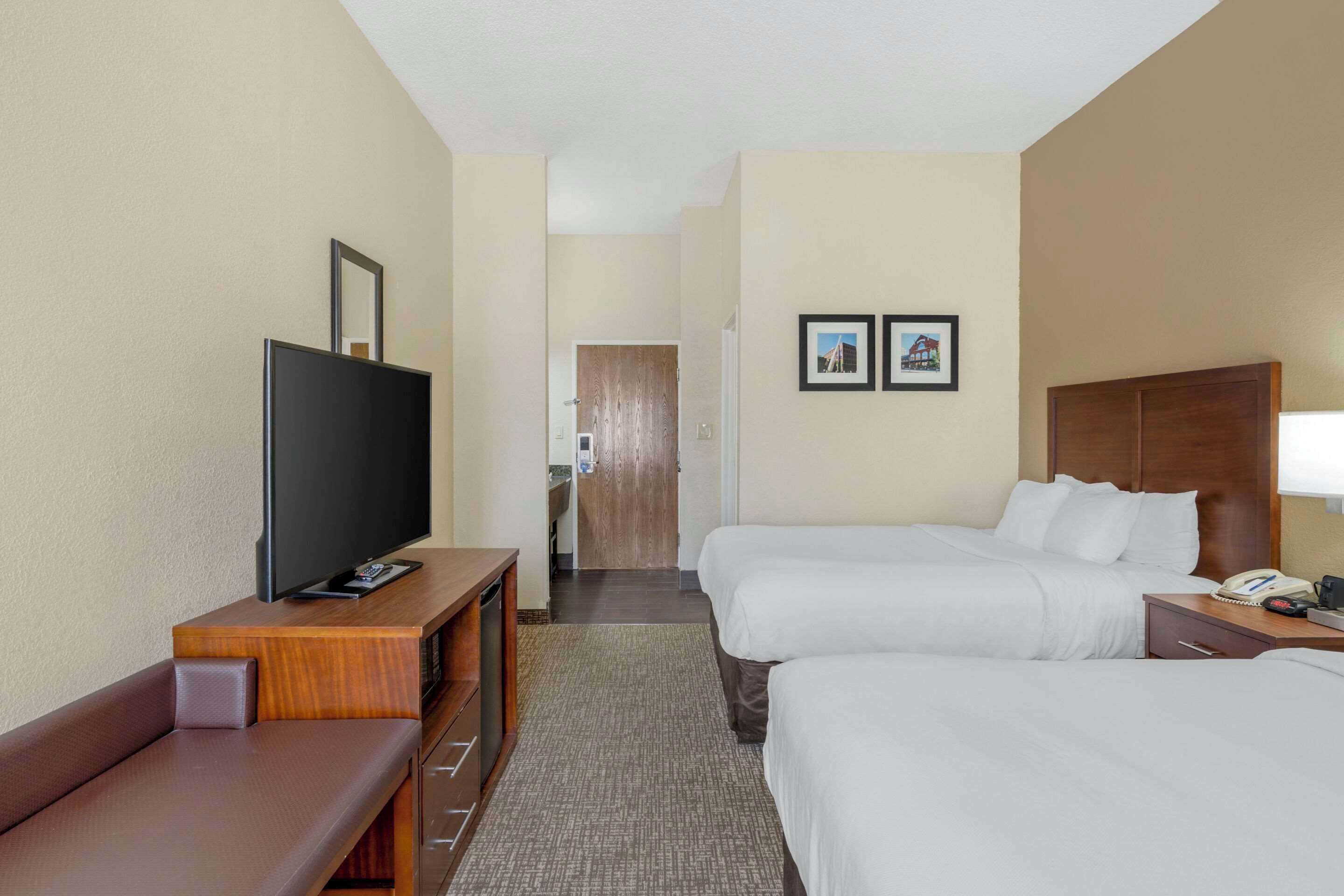 A hotel room with a TV, two beds, a desk, and a bathroom door in the background.