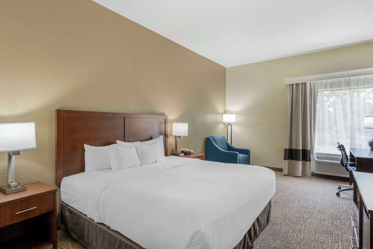 Una habitación de hotel con una cama grande, un escritorio, una silla y un ventanal con cortinas.