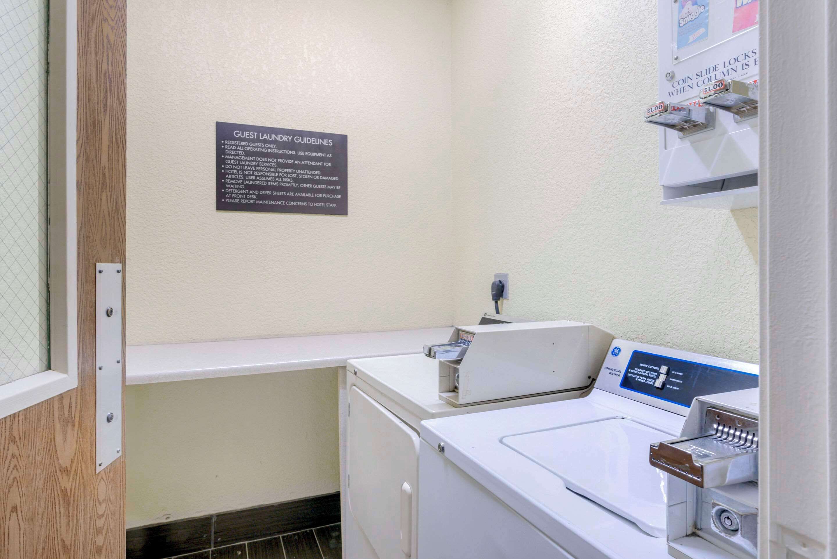 A laundry area with a sign detailing guest laundry guidelines, a coin-operated dryer, and a washing machine.