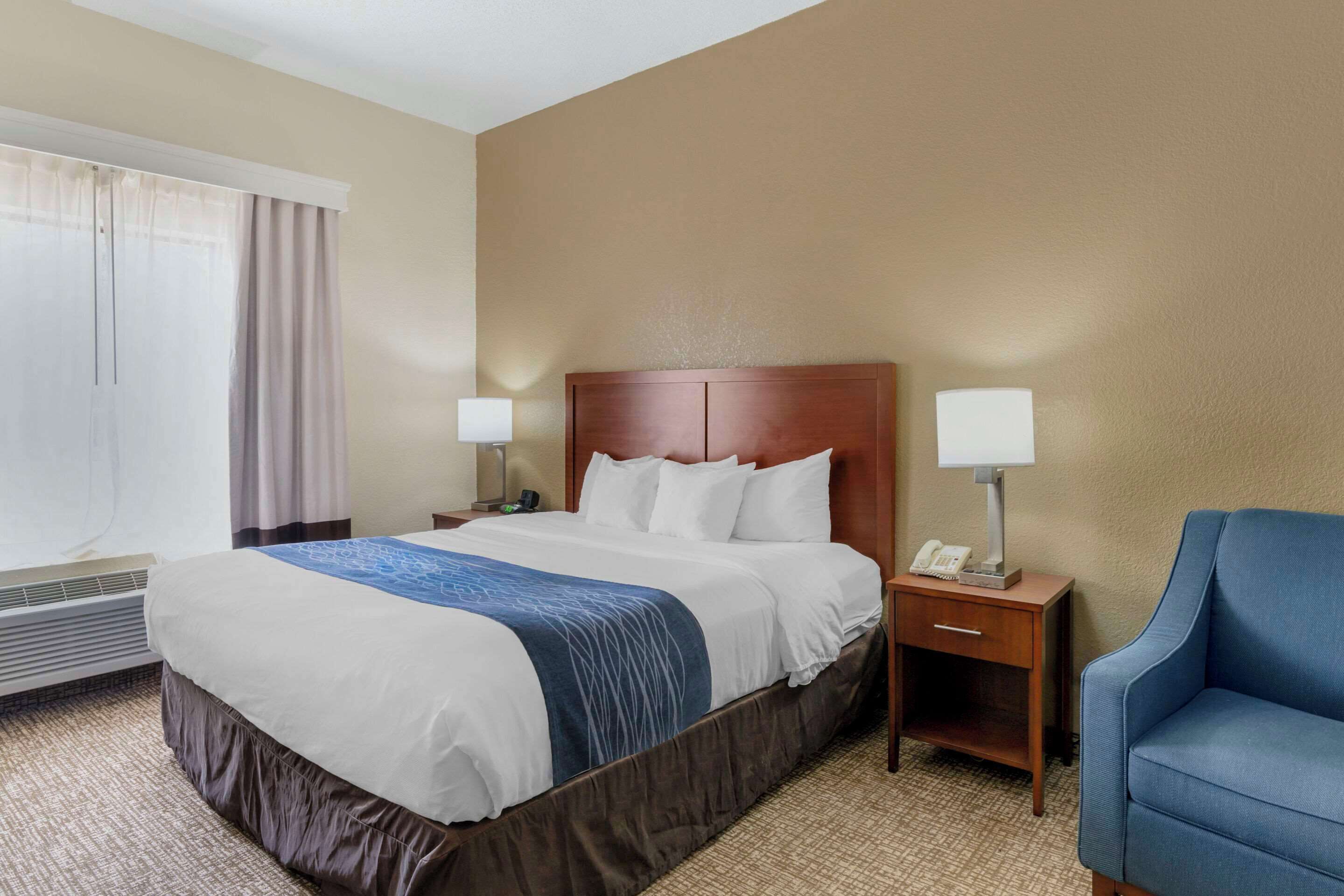 A hotel room with a large bed, two bedside tables with lamps, a chair, and a window with curtains.