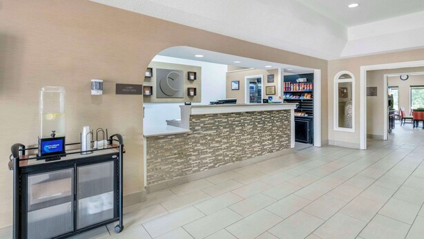 A reception area with a counter, a digital screen, and a cart with a water dispenser. - Comfort Inn & Suites La Grange - Louisville Area (La Grange)