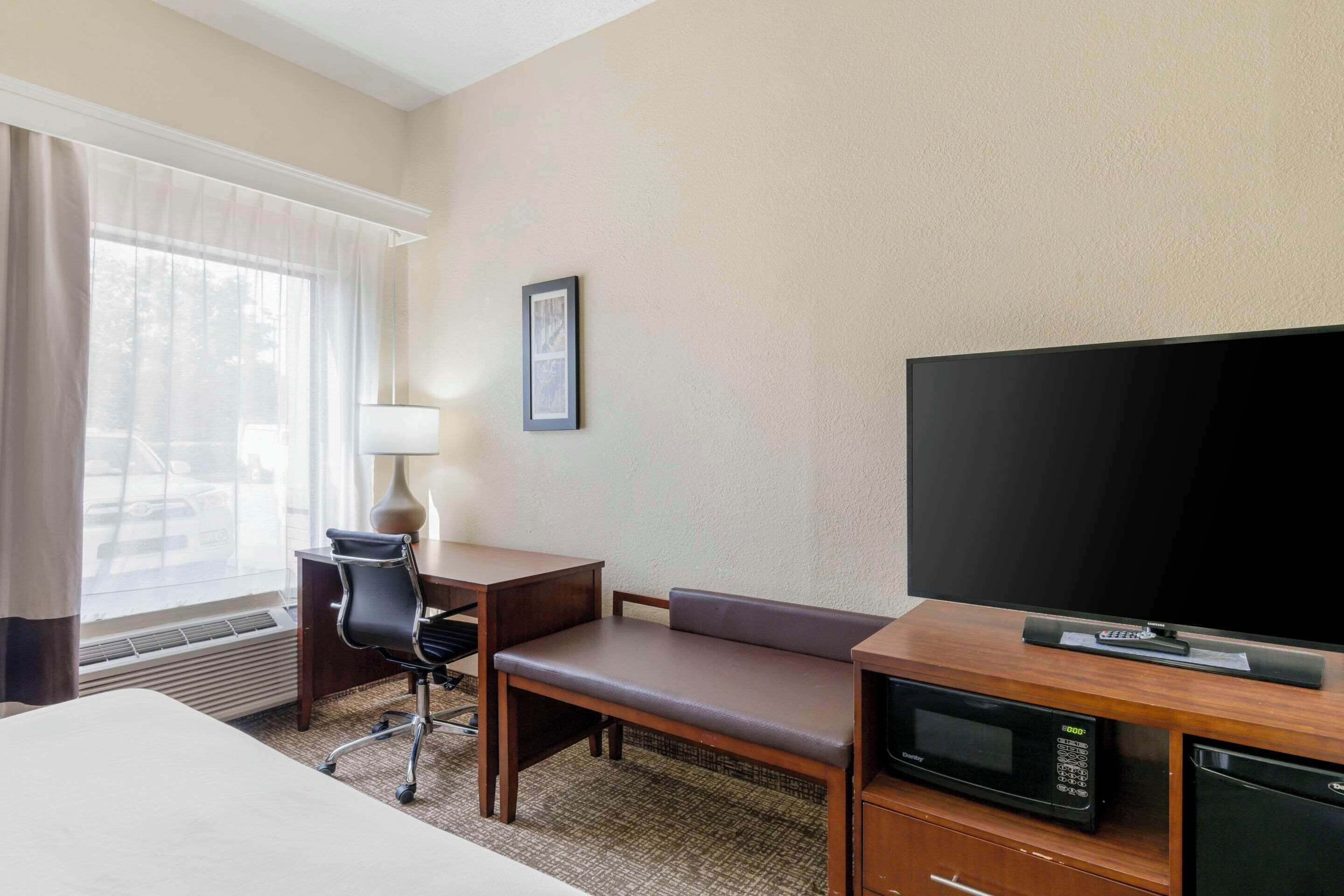 A hotel room with a bed, a desk with a chair, a television, a microwave, and a framed picture on the wall.