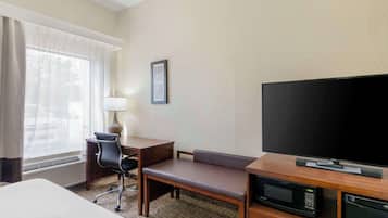 A hotel room with a bed, a desk with a chair, a television, a microwave, and a framed picture on the wall.