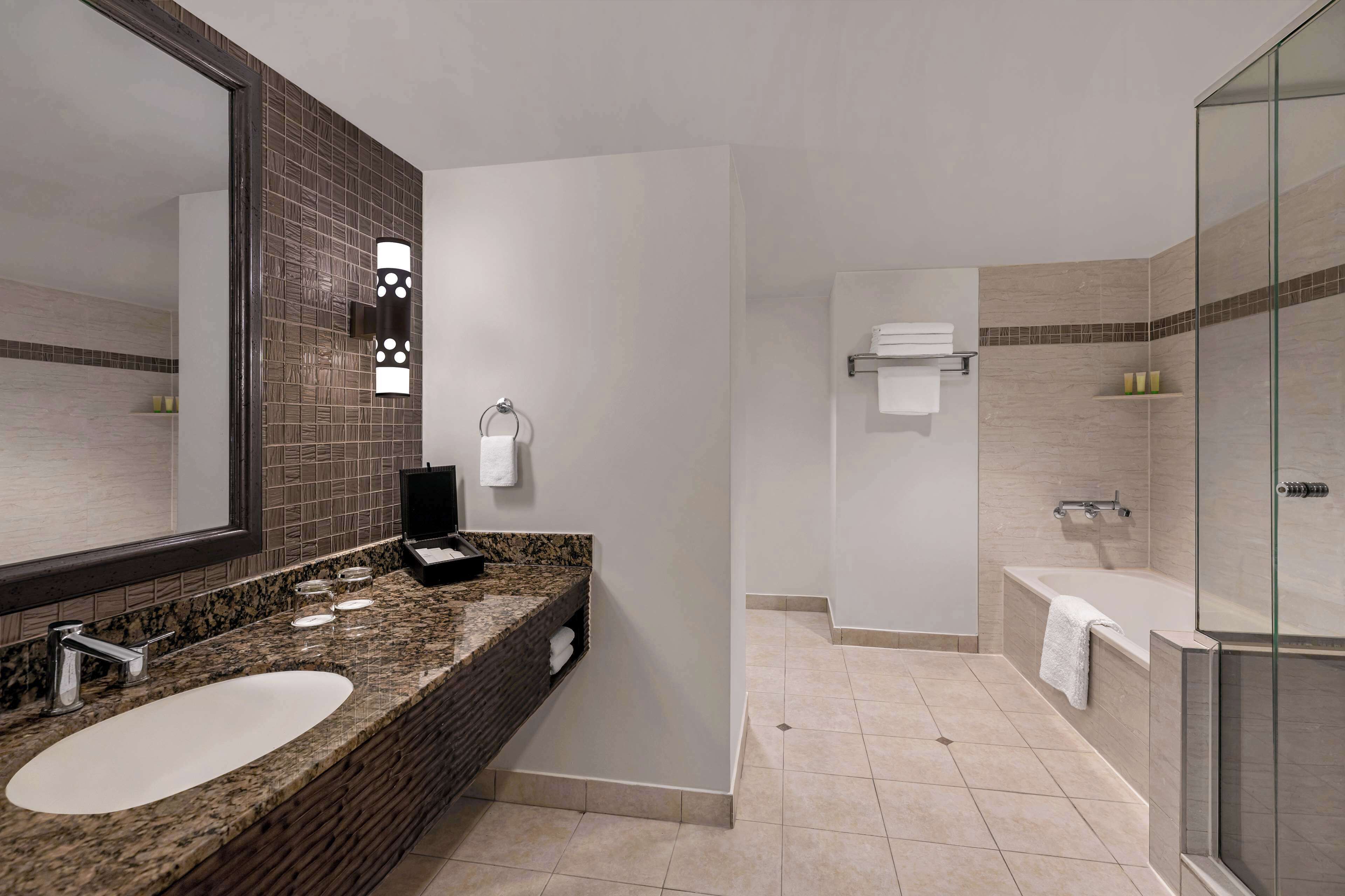 A modern bathroom with a granite countertop, a large mirror, a glass-enclosed shower, and a bathtub.