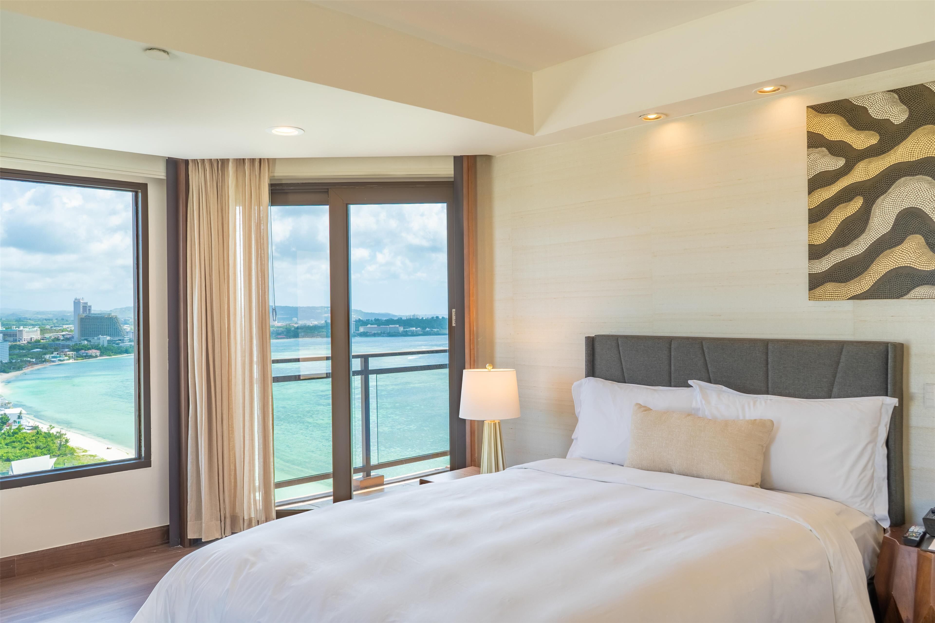 Ein Hotelzimmer mit einem großen Bett, Blick auf ein Gewässer und eine Stadtansicht.
