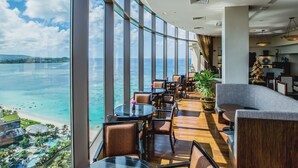 A high-rise hotel room with a panoramic ocean view, furnished with modern seating and a small table. - Dusit Beach Resort Guam (Tamuning)