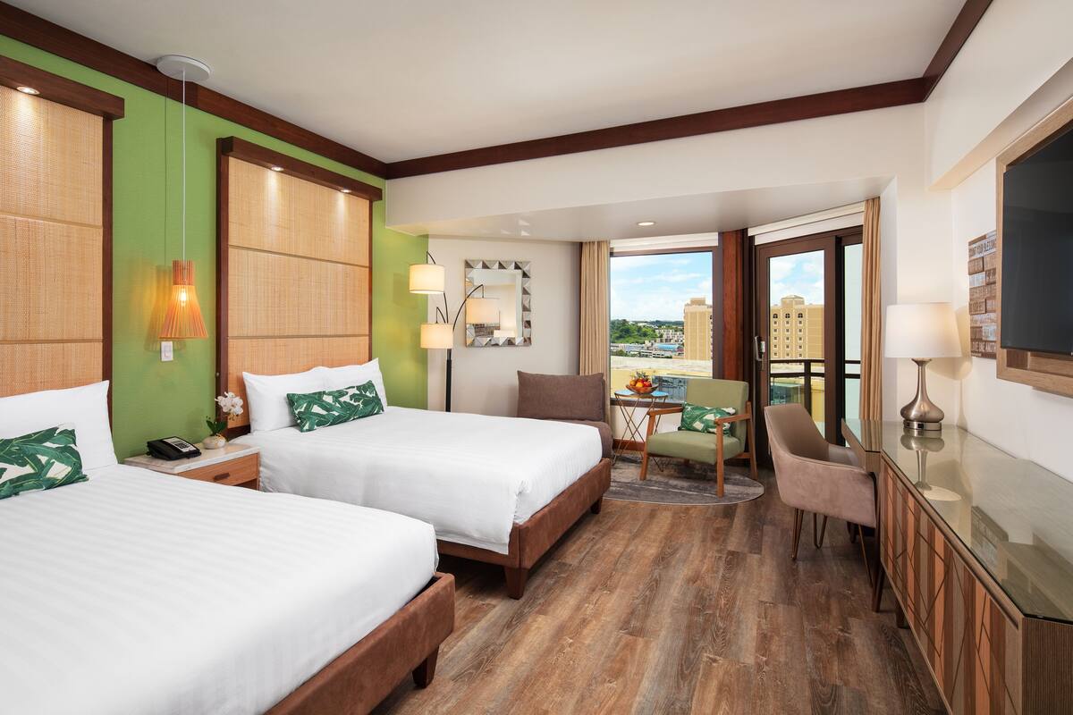 A hotel room with two beds, a sitting area with a table and chairs, and a balcony with a view.
