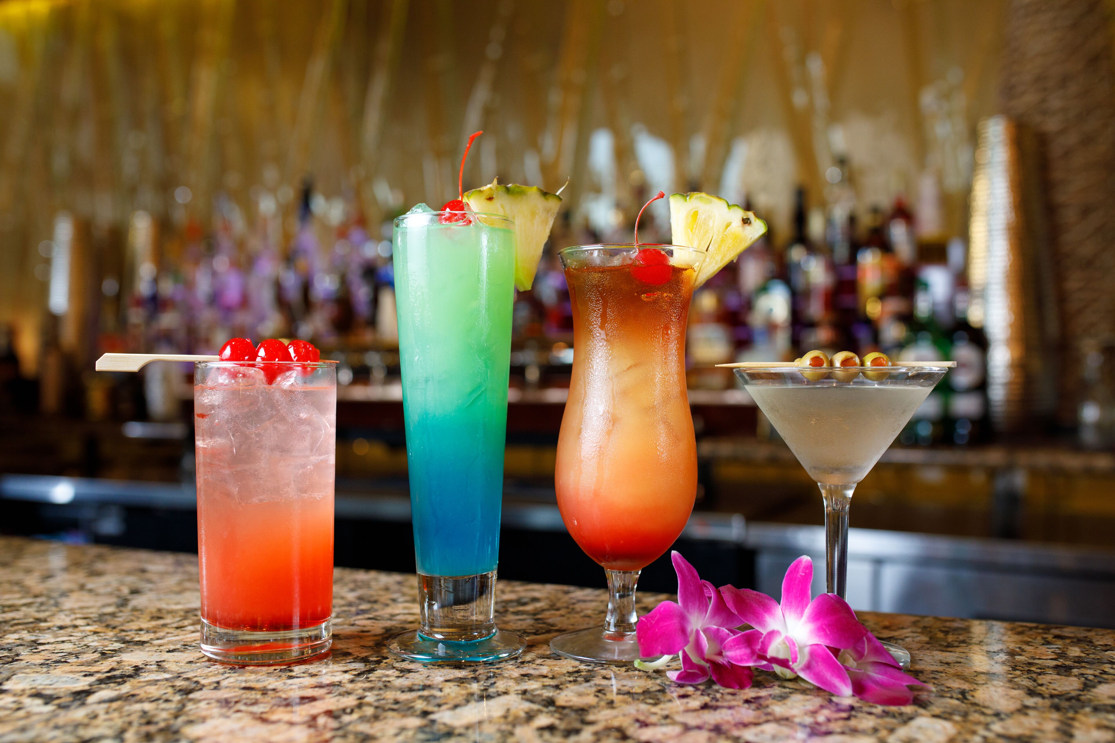 Trois cocktails sur un comptoir de bar, avec un arrière-plan flou composé de bouteilles.