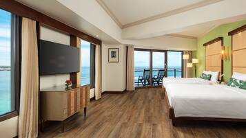 A hotel room with a large bed, a TV, a wooden cabinet, and a view of the sea.